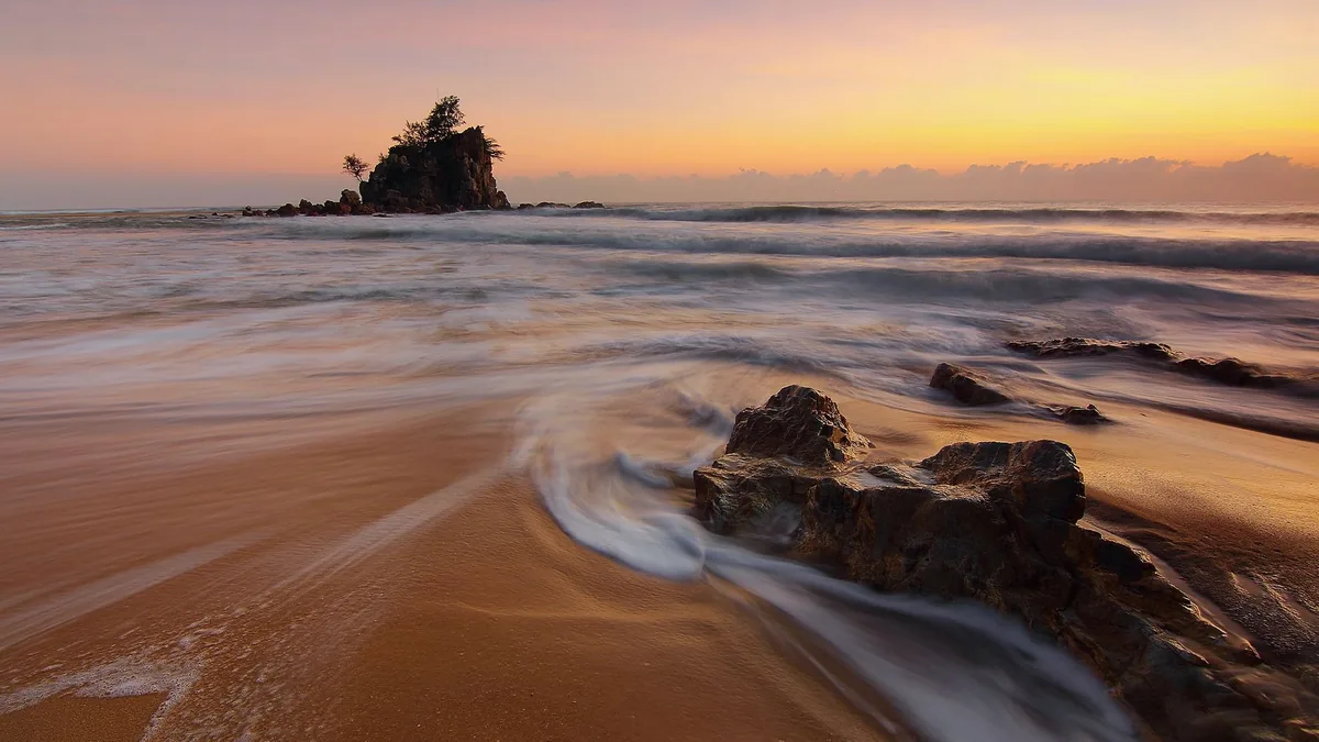 Peaceful beach scene with waves crashing on rocks at sunrise, capturing the beauty of nature.